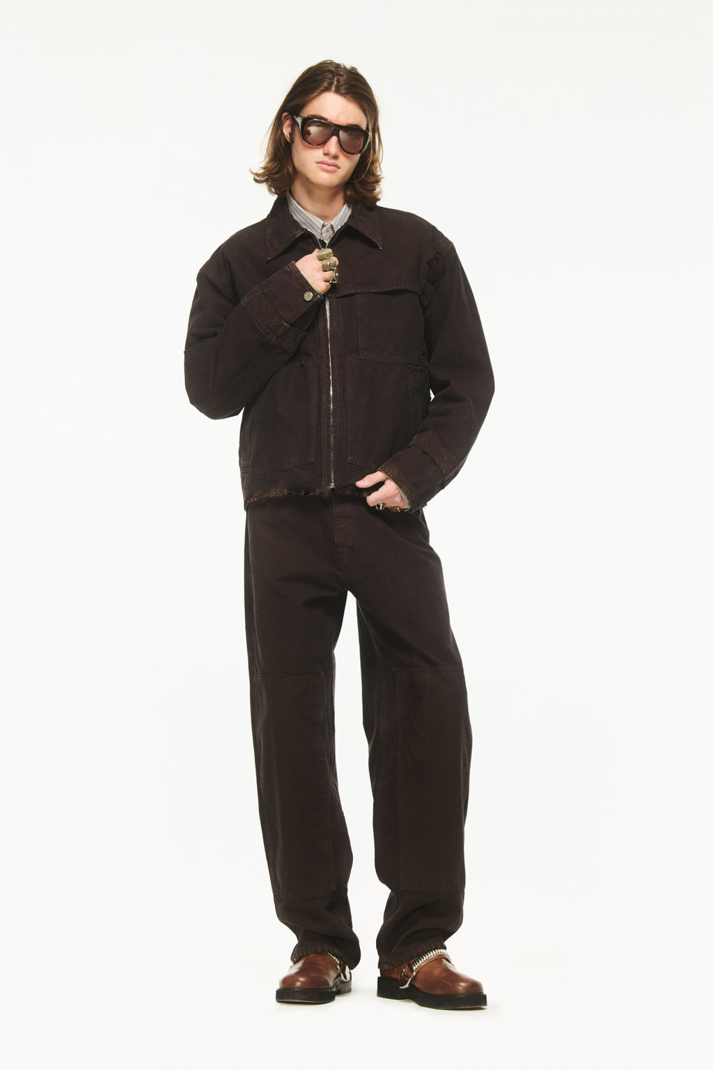 Male model wearing BLUEMARBLE garment-dyed brown canvas workwear pants featuring a relaxed fit, high-rise waist, knee patch panels, five-pocket construction, belt loops and zip fly closure.