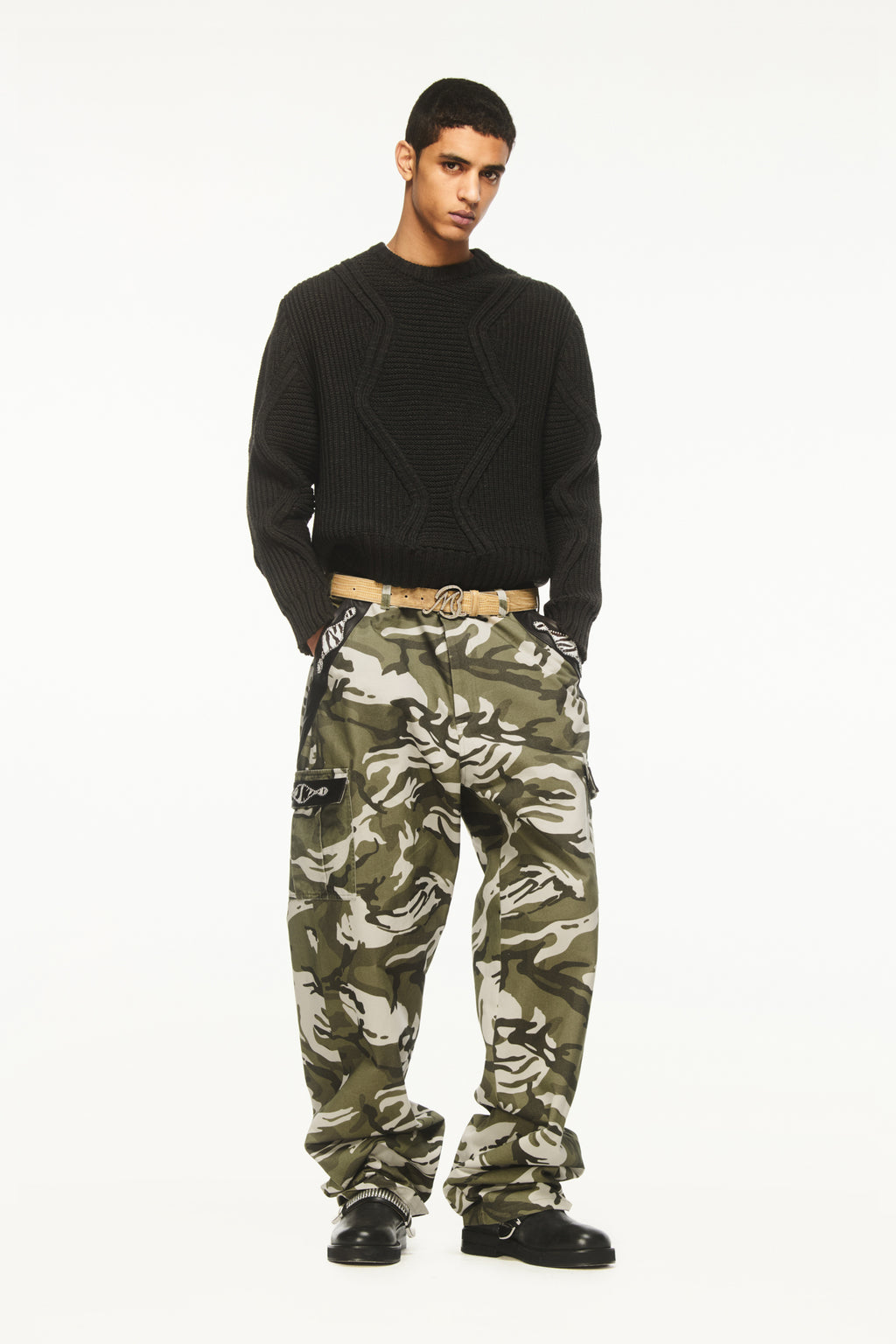 A male model wearing BLUEMARBLE camouflage cargo pants in soft-touch cotton twill featuring a relaxed fit, pony and leather detailing at the pockets, two side pockets, two cargo pockets, two back patch pockets and adjustable waist tabs styled with dark grey knitted jumper. 