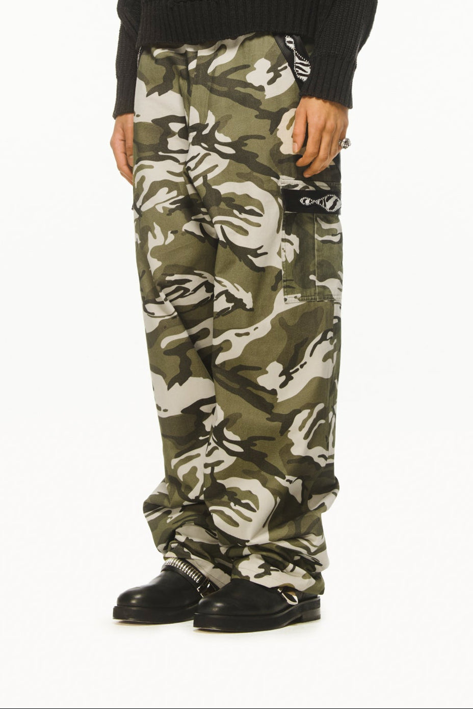 A male model wearing BLUEMARBLE camouflage cargo pants in soft-touch cotton twill featuring a relaxed fit, pony and leather detailing at the pockets, two side pockets, two cargo pockets, two back patch pockets and adjustable waist tabs styled with dark grey knitted jumper. 