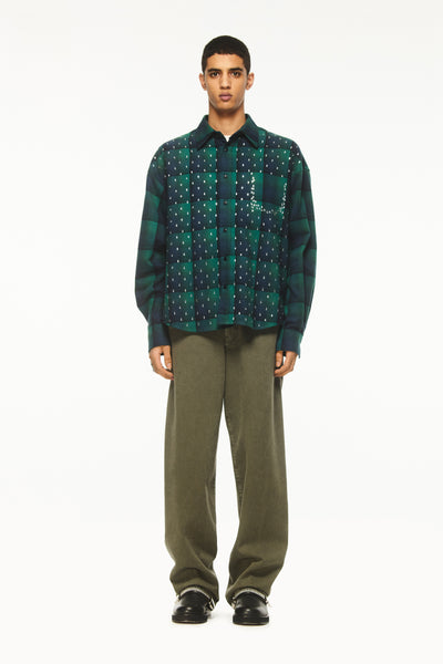 Male model wearing a BLUEMARBLE green and navy checked shirt in brushed cotton flannel, featuring rhinestone raindrop embellishments across the front, a slightly oversized fit and front button closure, styled with olive green trousers and black shoes against a white studio background.