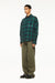 Male model wearing a BLUEMARBLE green and navy checked shirt in brushed cotton flannel, featuring rhinestone raindrop embellishments across the front, a slightly oversized fit and front button closure, styled with olive green trousers and black shoes against a white studio background.