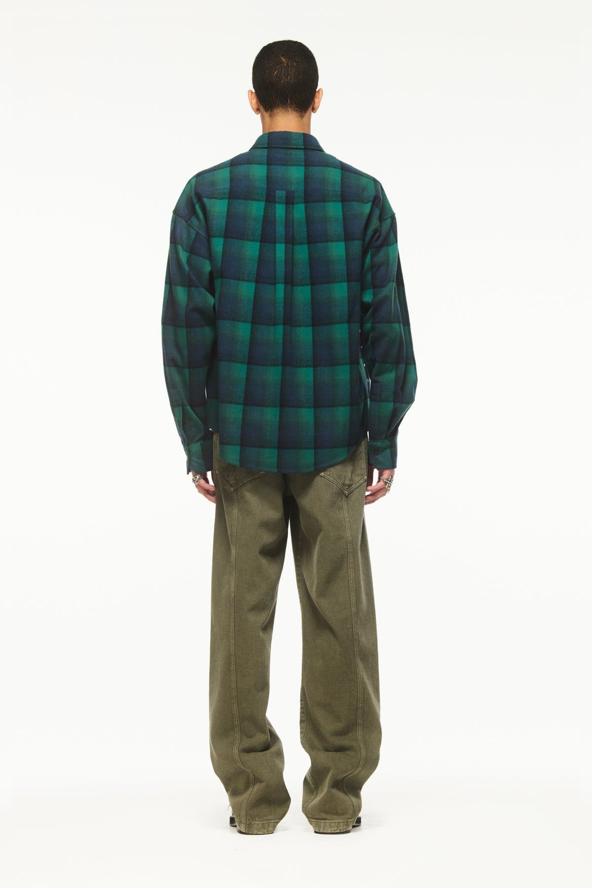 Male model wearing a BLUEMARBLE green and navy checked shirt in brushed cotton flannel, featuring rhinestone raindrop embellishments across the front, a slightly oversized fit and front button closure, styled with olive green trousers and black shoes against a white studio background.