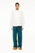 Male model wearing a BLUEMARBLE white poplin shirt featuring molten metal studs along the shoulders and armholes, raw-edge detailing and a slightly oversized fit, styled with duck green workwear pants against a white studio background.