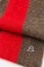 A close-up of Bluemarble folded knit scarf with bold red and brown stripes, featuring a small silver-tone BM logo on a white background.